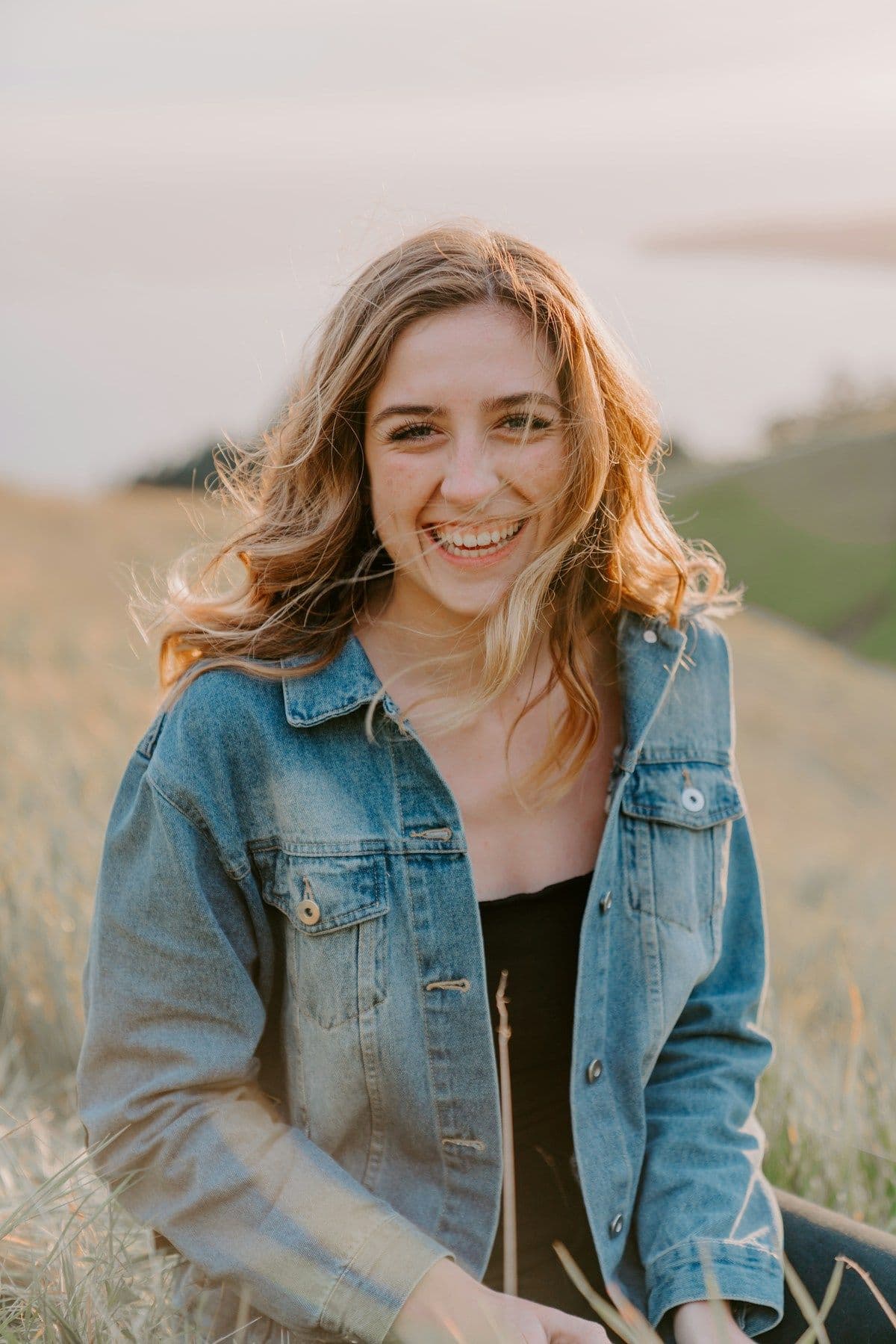 A woman in a denim jacket smiling in a sunlit field